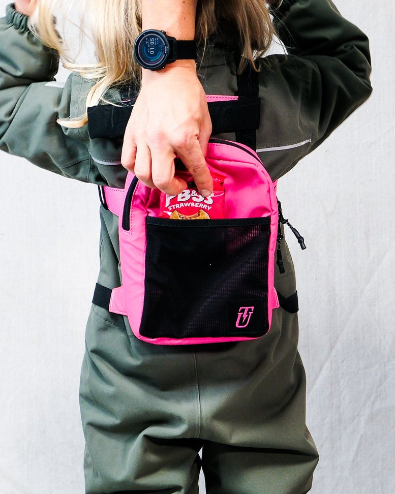 a kid wearing a pink ski harness backpack with snacks being placed inside