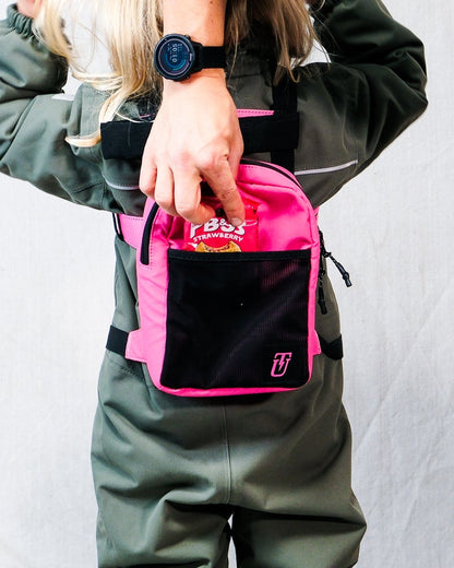 a kid wearing a pink ski harness backpack with snacks being placed inside